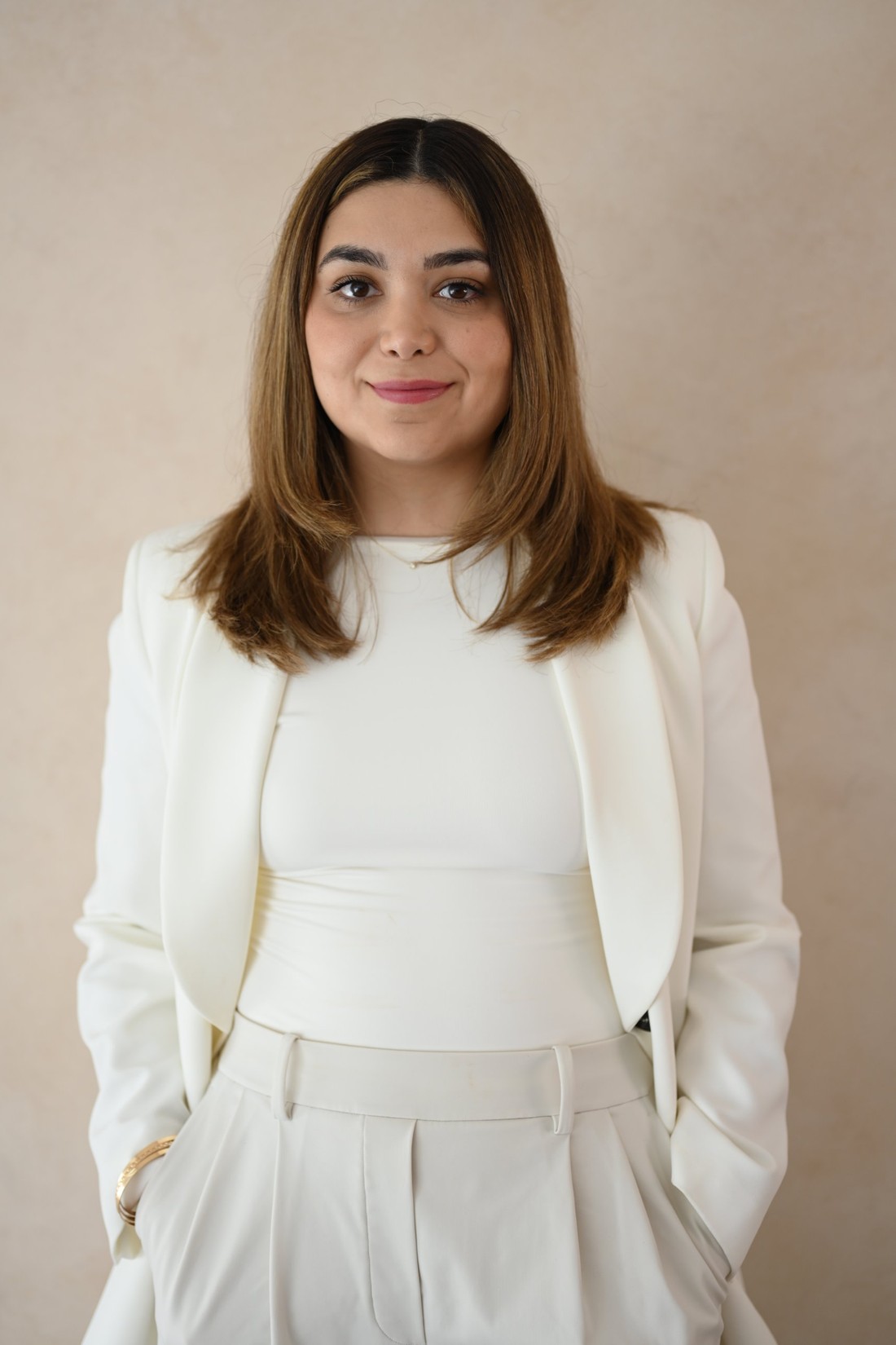 Psicóloga Nancy Mayorga con saco blanco y manos en los bolsillos sobre fondo arena